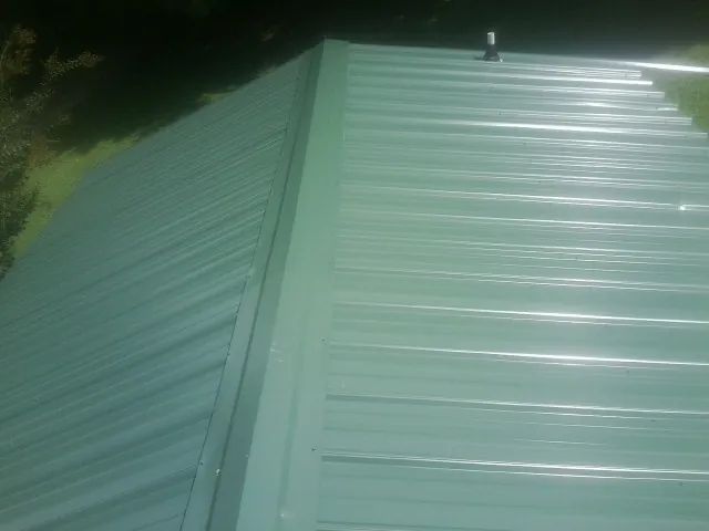 New green metal panels meeting at the ridge of a roof — Flat Roof Repair work by our crew in Lawrence