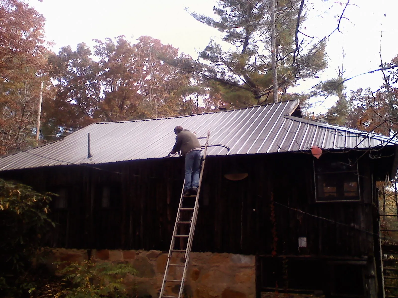 Roofer on a ladder working along the edge of a cabin metal roof in Lawrence